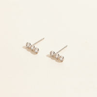 Pair of silver earrings with clear stones on a beige background