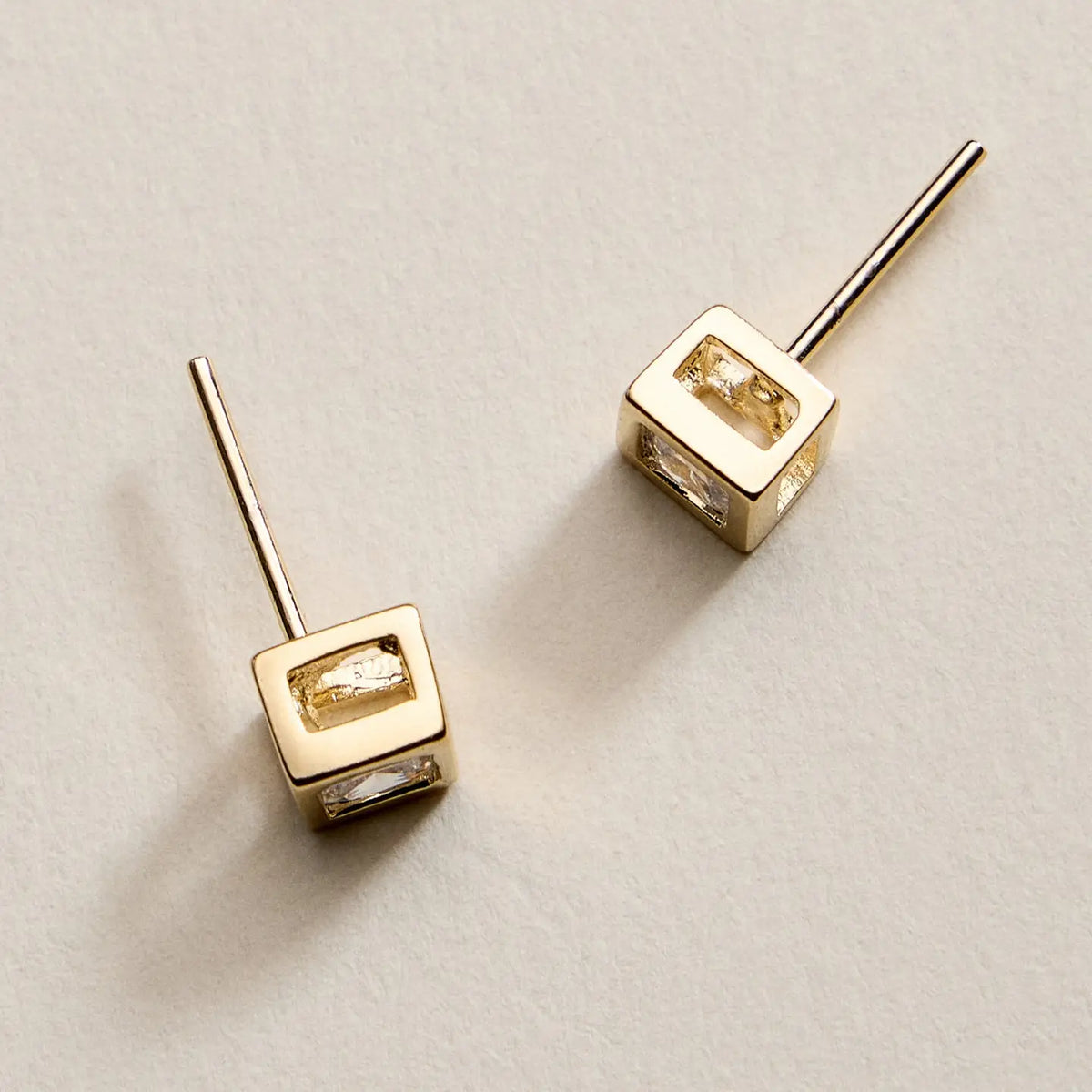 Gold square earrings on a light beige background