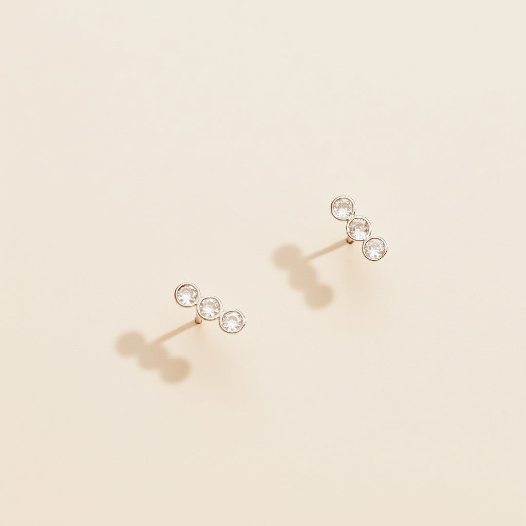 Pair of gold earrings with clear gemstones on a beige background