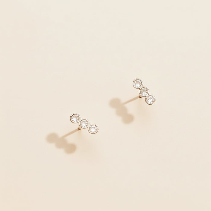 Pair of gold earrings with clear gemstones on a beige background