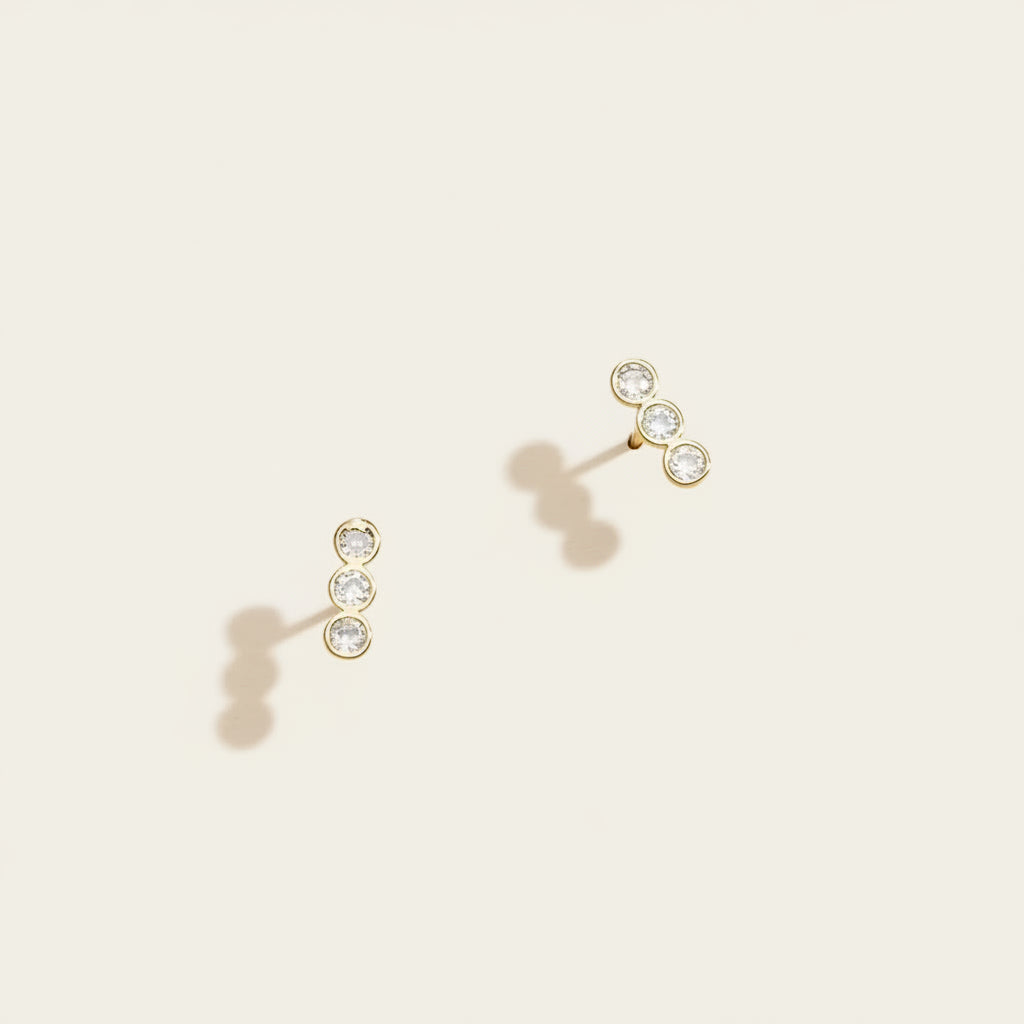 Pair of gold earrings with clear gemstones on a beige background