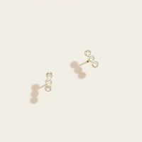 Pair of gold earrings with clear gemstones on a beige background