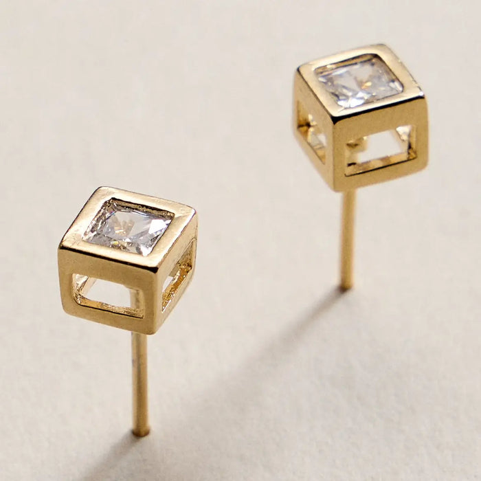 Gold square earrings with clear gemstones on a beige background