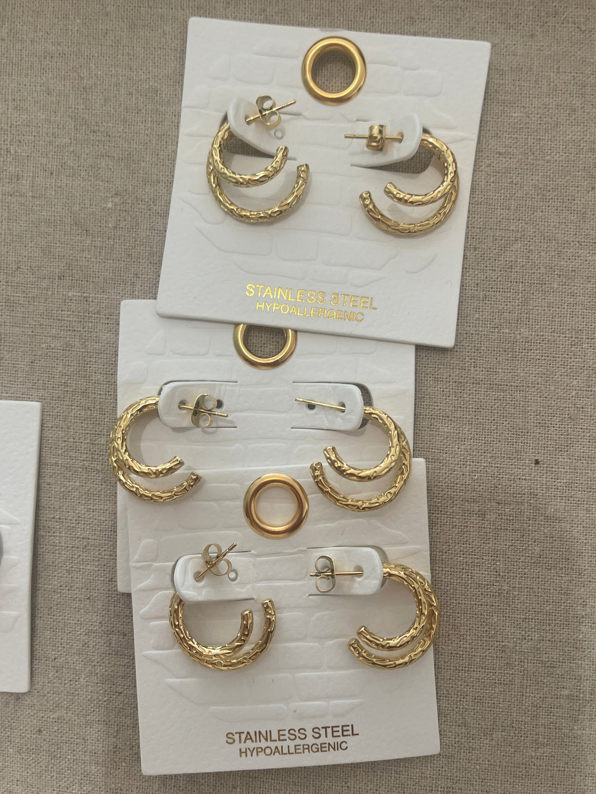 Gold earrings on white cards with '925 Sterling Silver' text on a beige fabric background