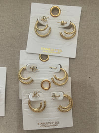 Gold earrings on white cards with '925 Sterling Silver' text on a beige fabric background