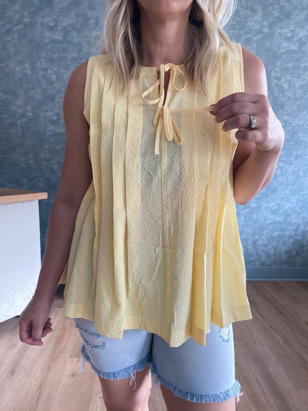 Person wearing a yellow sleeveless top with a blue wall background