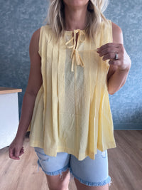 Person wearing a yellow sleeveless top with a blue wall background