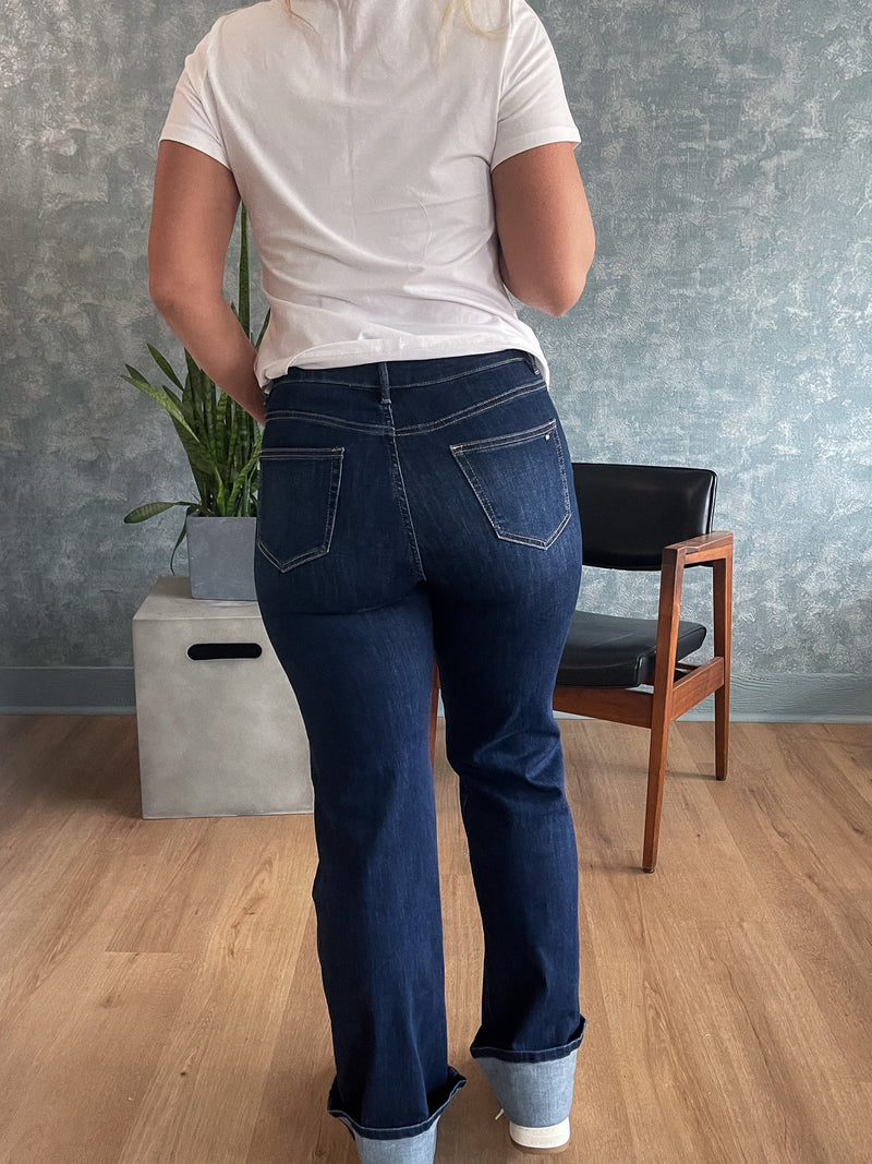 Person wearing blue jeans and a white shirt in a room with a chair and plant.