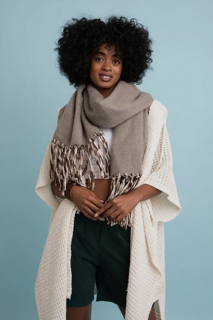Woman wearing a beige scarf, white top, and dark shorts against a light blue background