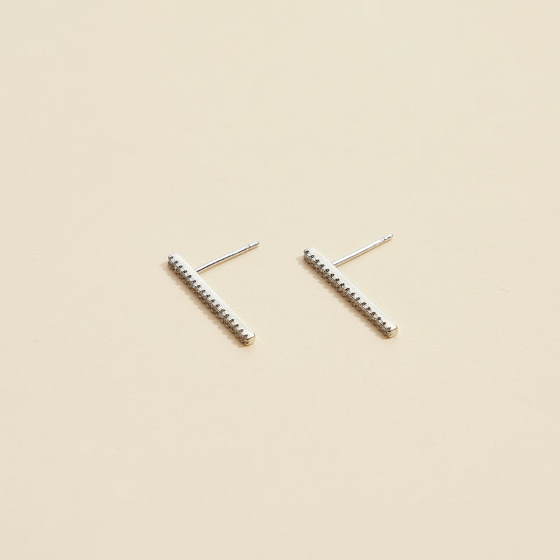 Pair of silver bar earrings on a beige background
